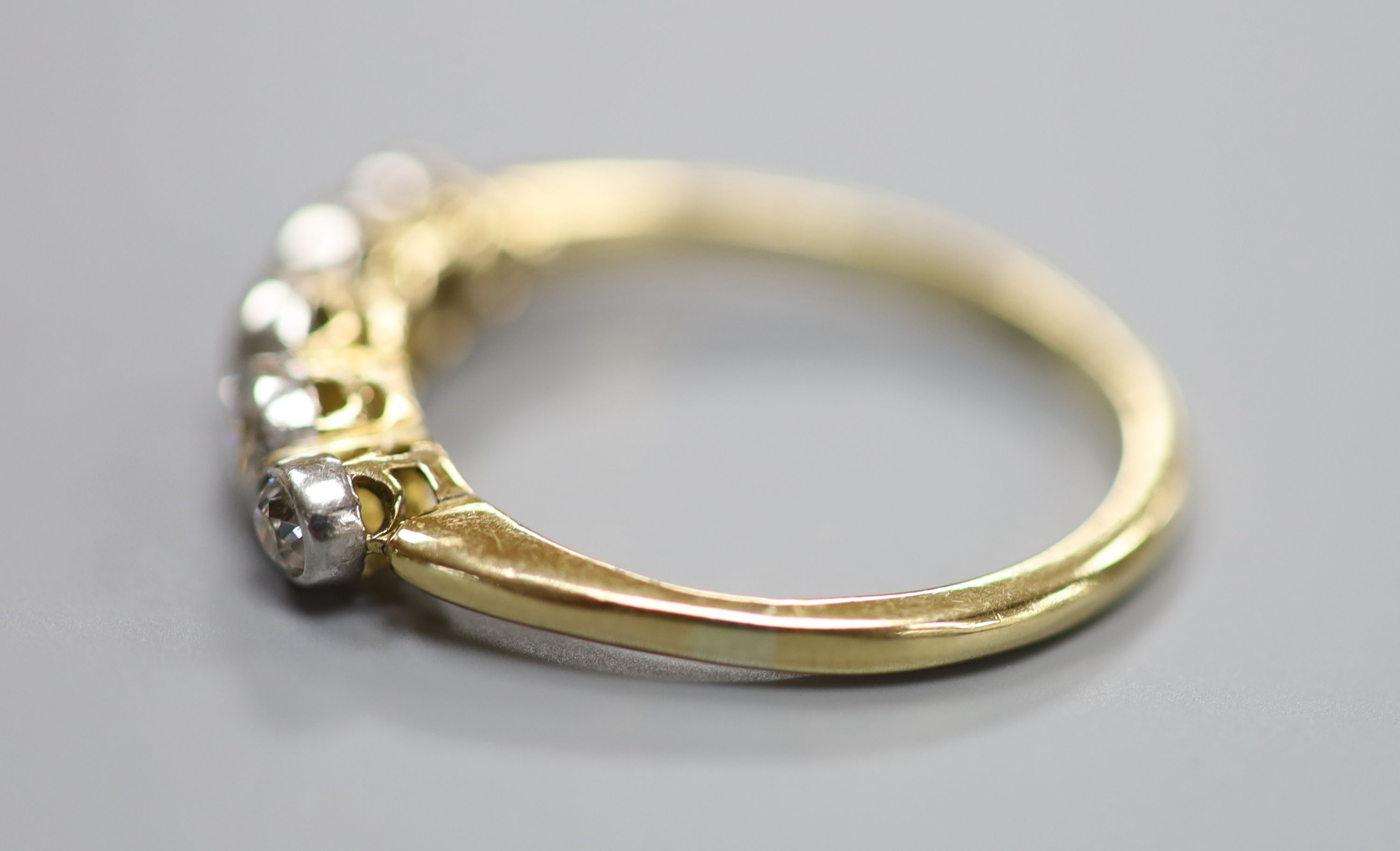 A yellow metal and graduated five stone diamond set half hoop ring, size P/Q, gross 2.6 grams.